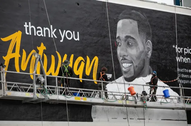 Four Open Air Gallery painters on a suspended platform, finishing a painted portrait wall