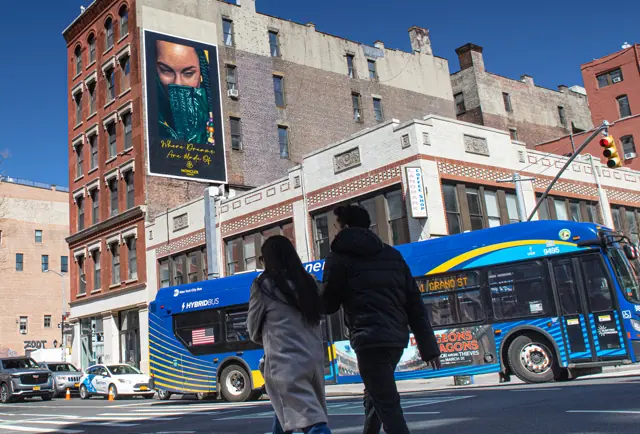 A hand-painted wall advertisement high above a New York street, with traffic and pedestrians below it for scale